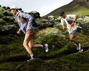 Eine Läuferin und ein Läufer auf beim Trailrunning in einer Berglandschaft. Die beiden sind ausgerüstet mit Laufbekleidung, Laufschuhen und Laufausrüstung von Salomon.