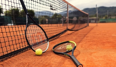 Ein Tennisschläger der Marke Wilson lehnt am Netz, am Boden liegt ein Tennisschläger der Marke Dunlop.